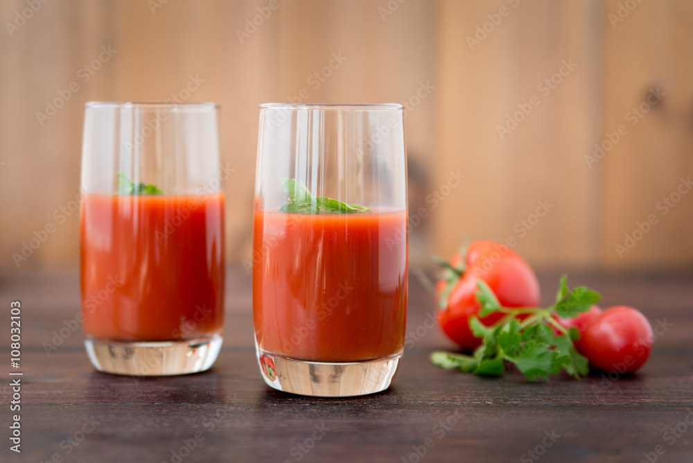 Glass of tomato juice with vegetables on old wooden background, with greenery and tomatoes