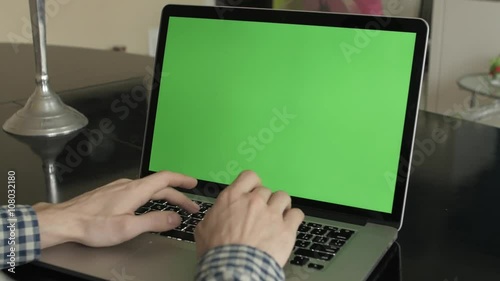 A man types on a laptop on his desk.  Green screen for your custom screen content.