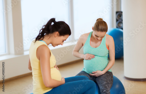 two happy pregnant women sitting on balls in gym