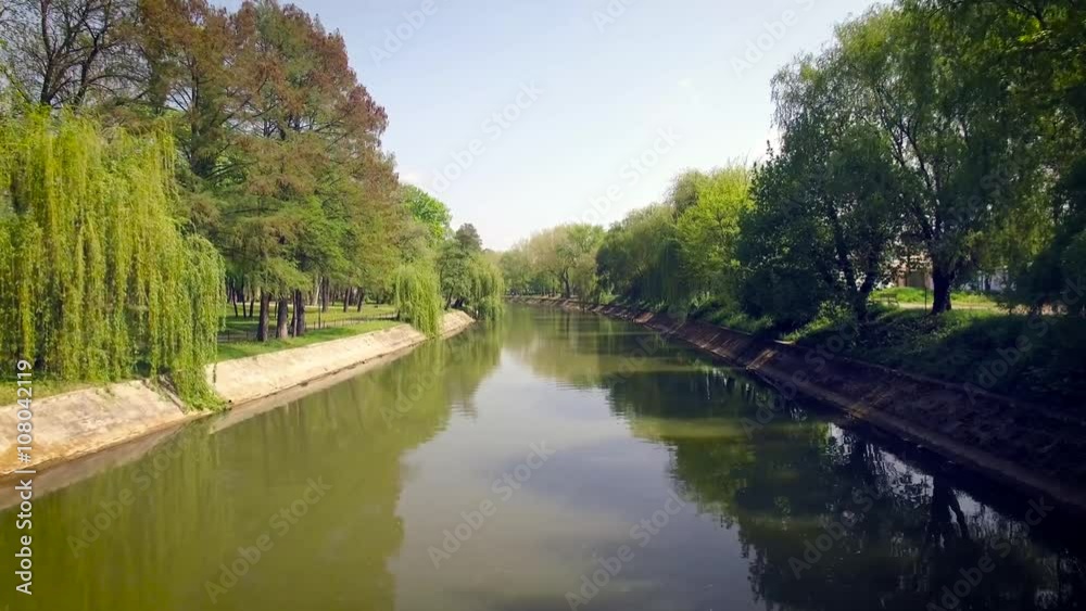 Drone flying over a river with many green trees on the edge, Bega channel, Timisoara Drone flying over a river with many green trees on the edge, Bega channel, Timisoara