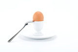 Boiled egg in egg cup on dish with spoon, on white background.