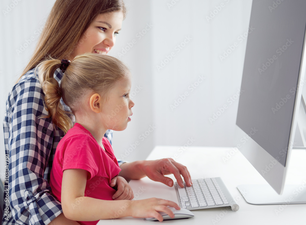 Children education. Young mother teaching her little daughter sitting at the desk in front of computer in homeoffice. Children education. Young mother teaching her little daughter sitting at the desk in front of computer in homeoffice.