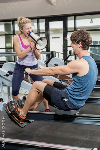 Trainer yelling through a megaphone while man on rowing machine