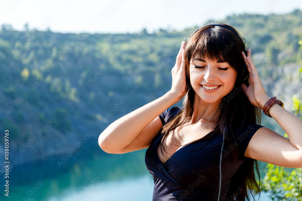 Smiling brunette girl with long hair listening the music on the background of mountain river