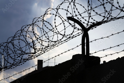 Fotografia Dramatic clouds behind barbed wire fence on a prison wall