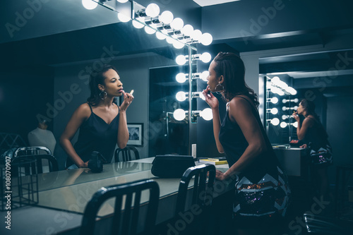 Black woman applying makeup in vanity mirror photo
