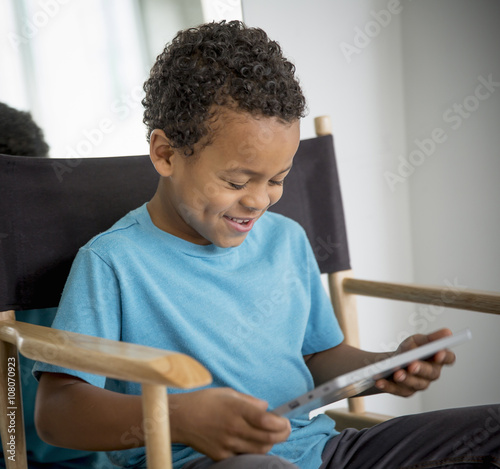 Mixed race boy using digital tablet in directors s chair photo