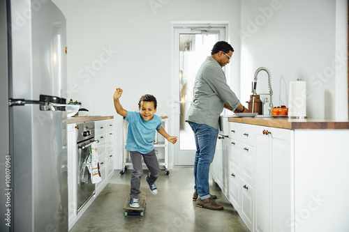 Boy skateboarding near father in kitchen photo