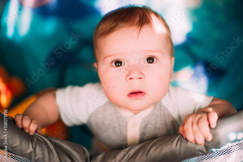 Cute little baby boy playing in colorful playpen, indoors. Beautiful child having fun at nursery.