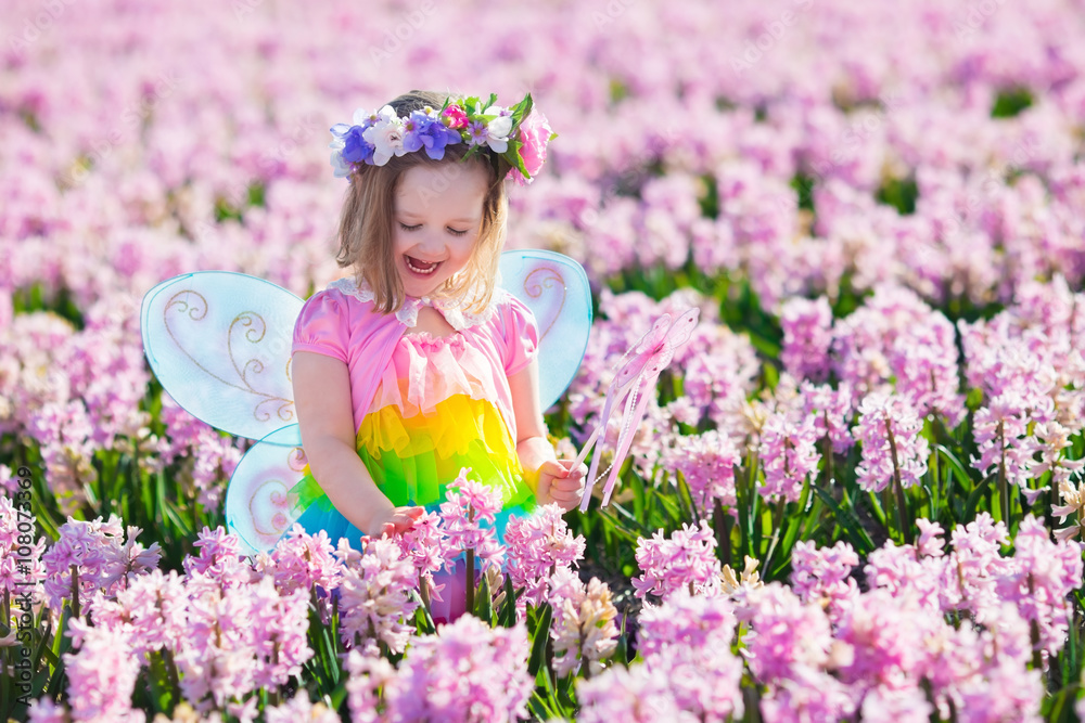 Beautiful girl playing in blooming hyacinth flower field. Kids princess birthday party with fairy costume, butterfly wings and magic wand. Children play in spring flowers. Child picking hyacinths.