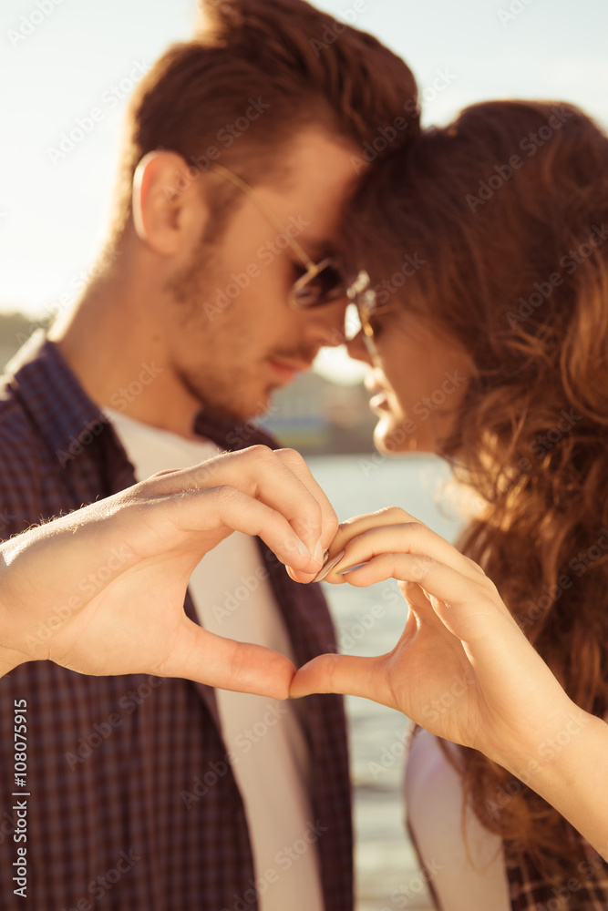 Fototapeta premium Romantic couple in love gesturing a heart with fingers at sunset