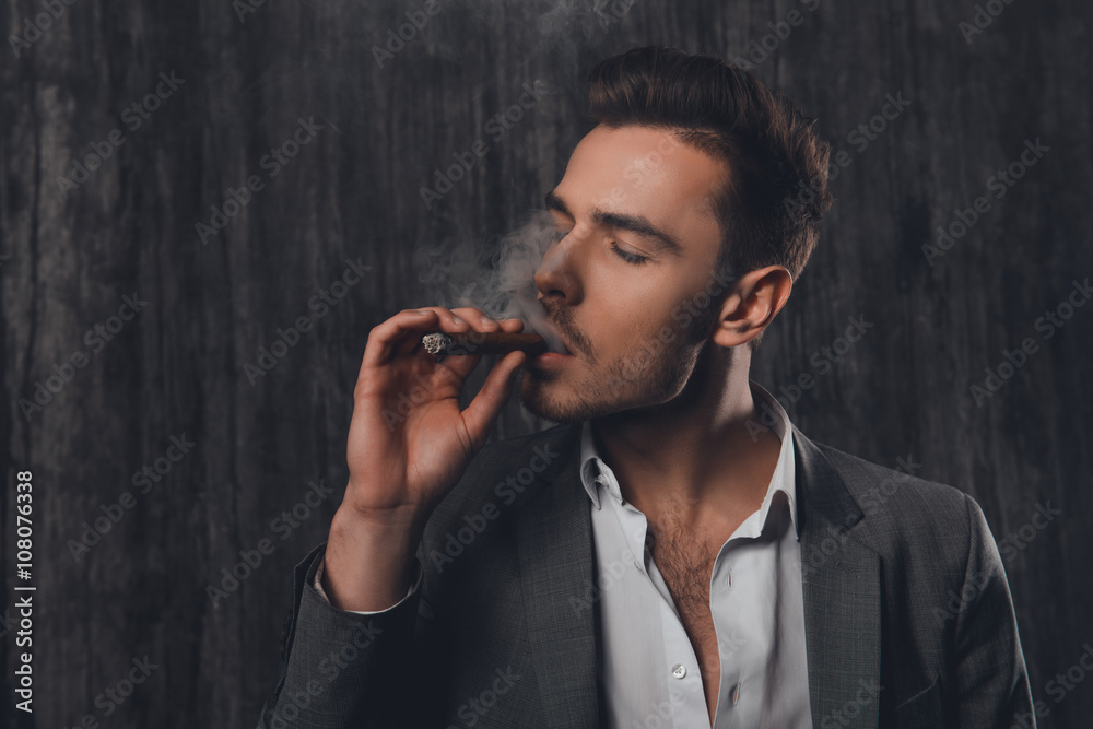 Portrait of successful young businessman in suit smoking a cigar