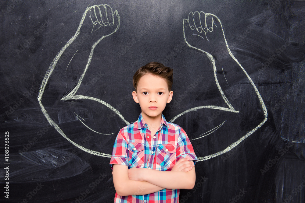 Little boy on backgroung of blackboard with drawn muscles