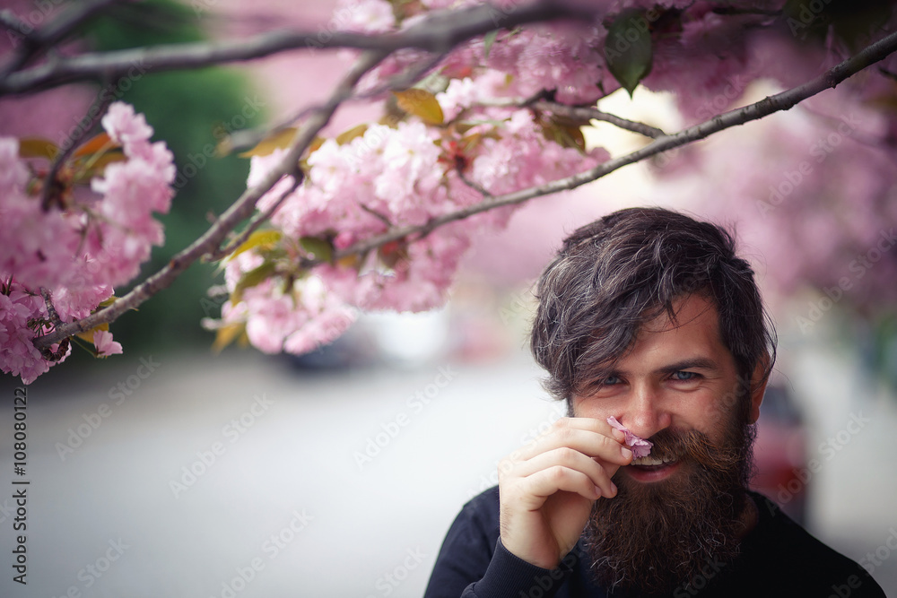 brutal bearded man brunette in a black blouse with elegant mustache and graying hair near the flowering cherry trees brutal bearded man brunette in a black blouse with elegant mustache and graying hair near the flowering cherry trees