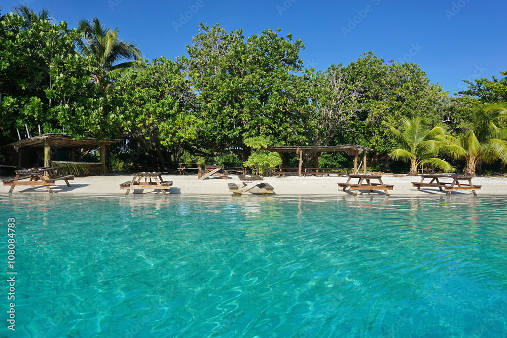 Picnic tables on a tropical beach with turquoise water on the shore of an islet, Huahine island, French Polynesia