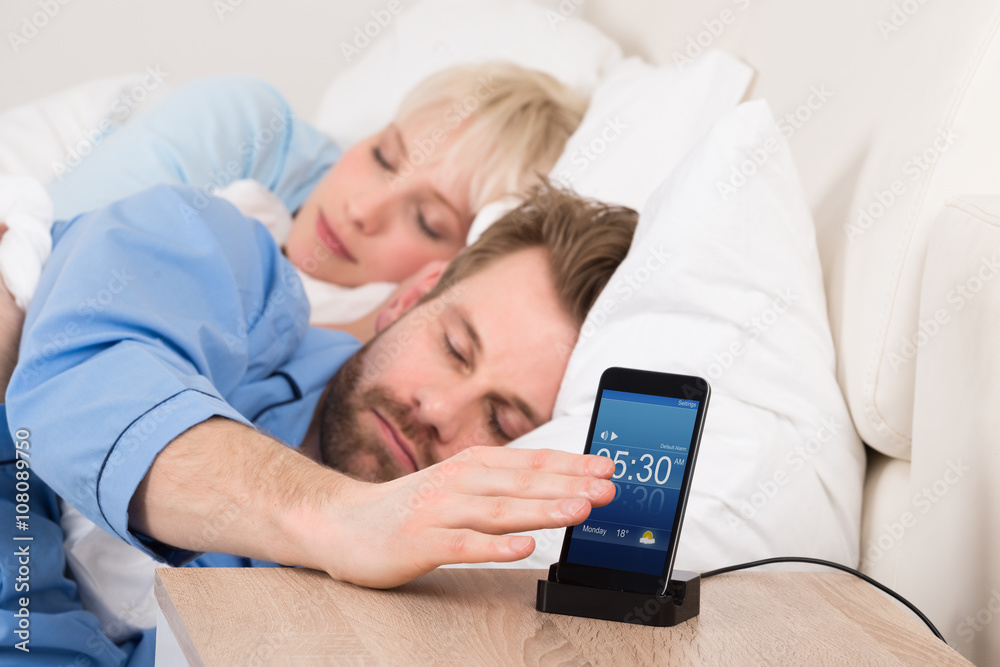 Man On Bed Snoozing Alarm Clock On Cell Phone Man On Bed Snoozing Alarm Clock On Cell Phone