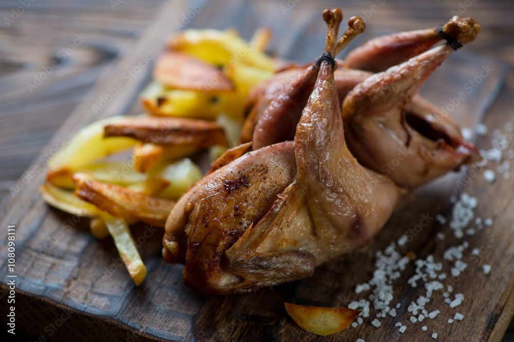 Whole baked quails with potato wedges, close-up, selective focus