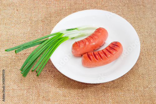 Photography Grilled sausages and green onion on white dish on sackcloth