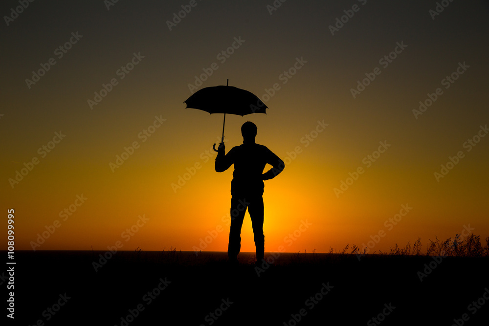 Man holding and umbrella in silhouette against  orange sunset