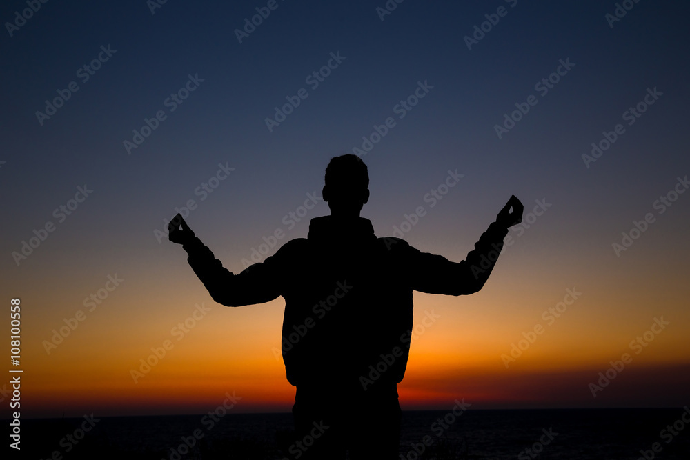 Silhouette of a man practicing yoga on a grassy horizon after su