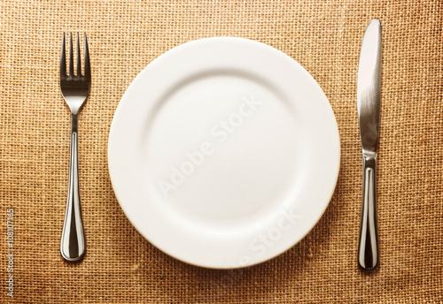 Photo of the fork and knife with white plate on sacking