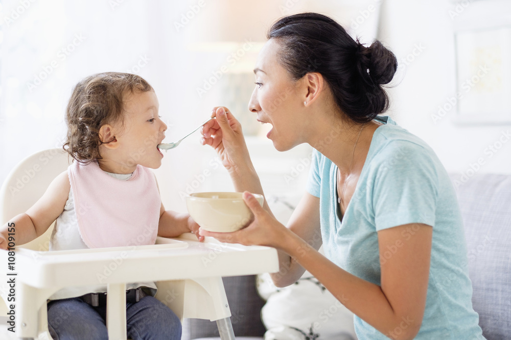 Mother feeding baby daughter in high chair Mother feeding baby daughter in high chair