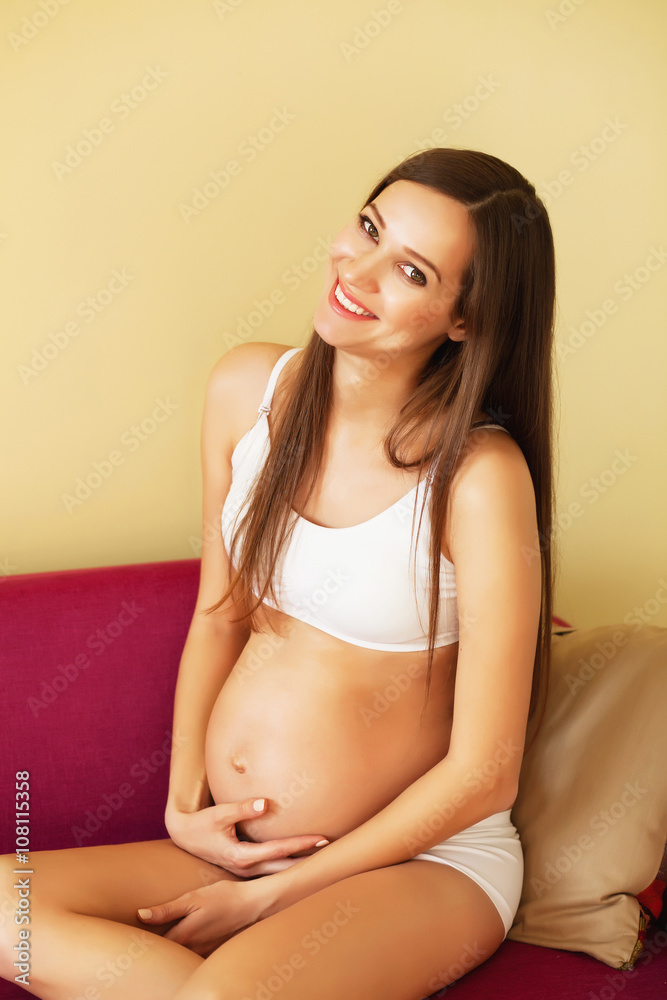 Lovely cheerful pregnant woman sitting on the sofa Lovely cheerful pregnant woman sitting on the sofa