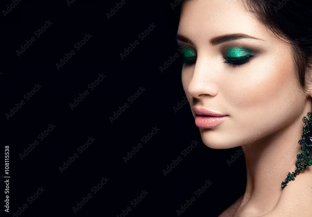 Beautiful woman portrait isolated on black background. Young lady posing with green eye shadows and earrings. Glamour make up. White skin. Beautiful woman portrait isolated on black background. Young lady posing with green eye shadows and earrings. Glamour make up. White skin.