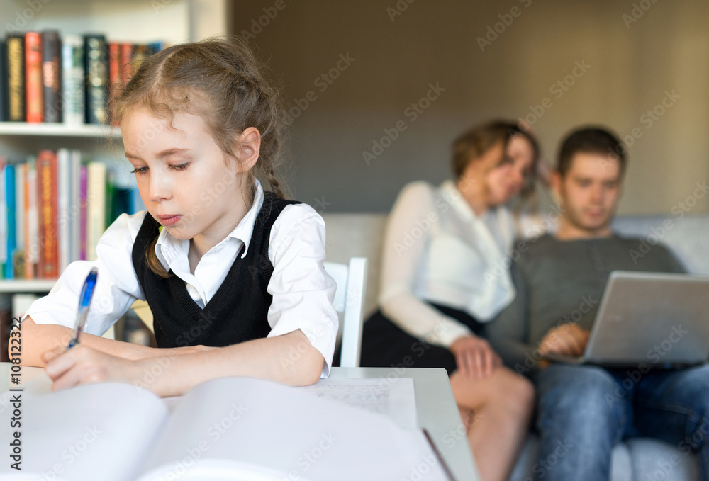 Little girl doing homework, while her parents resting on the sofa. Little girl doing homework, while her parents resting on the sofa.