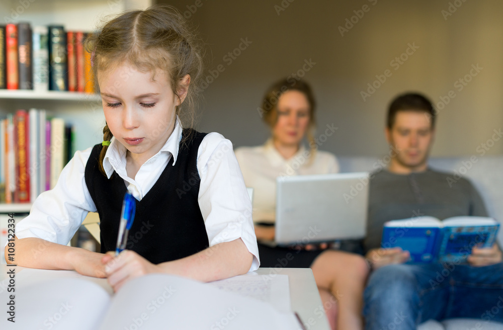 Little girl doing homework, while her parents resting on the sofa. Little girl doing homework, while her parents resting on the sofa.