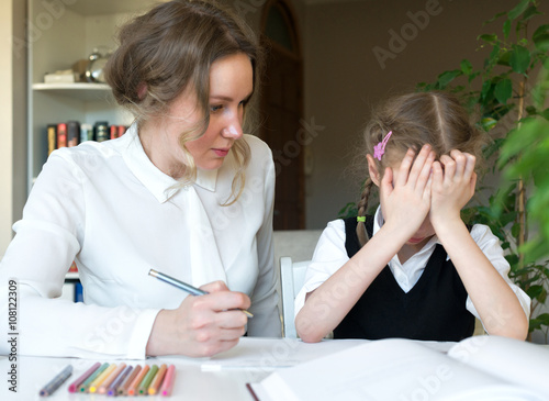 Mother helping her tired daughter with homework at home.