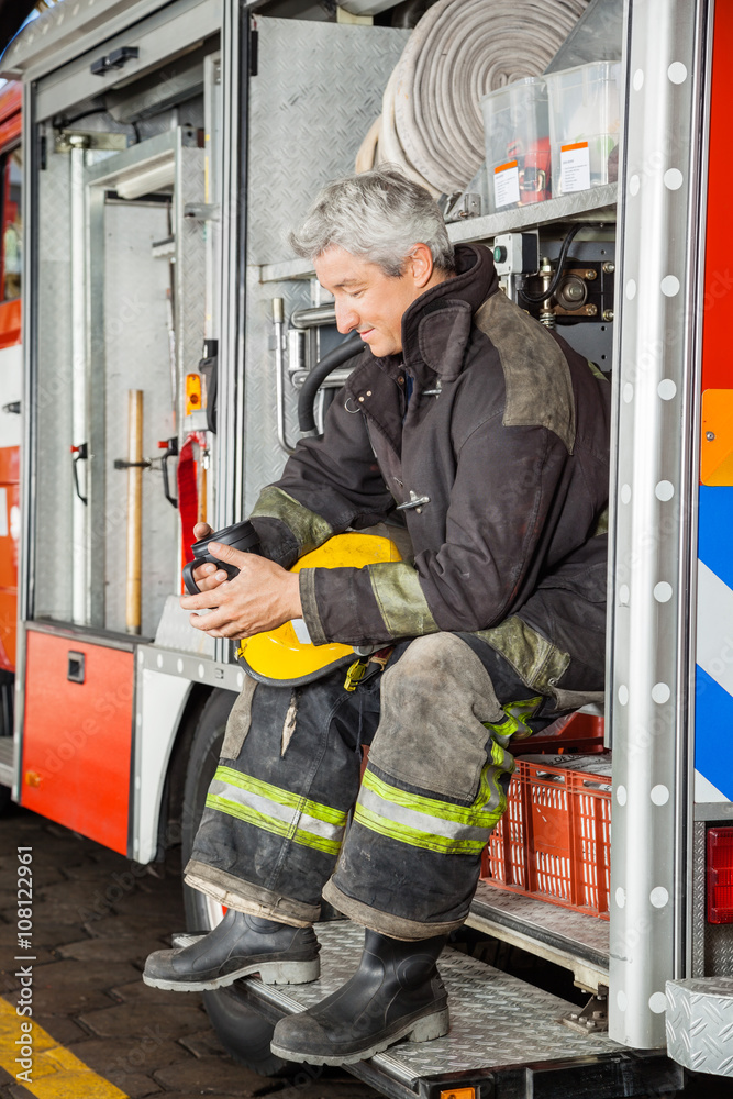 Fototapeta premium Smiling Fireman Looking At Coffee Mug While In Truck