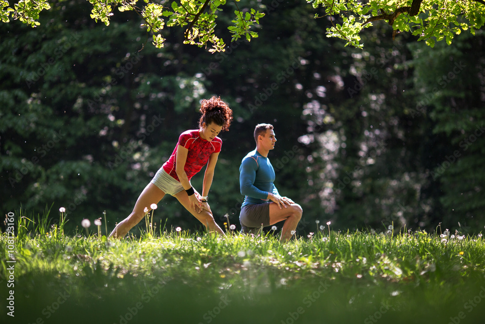 Fototapeta premium In the midst of nature's tranquility, a young couple takes a moment to stretch after jogging, embracing the serene ambiance that surrounds them.