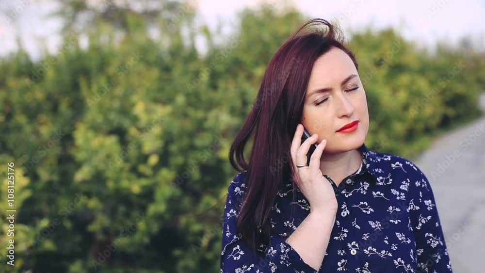 Woman talking on cellphone in the park and looking at the camera with smile. Woman talking on cellphone in the park and looking at the camera with smile.