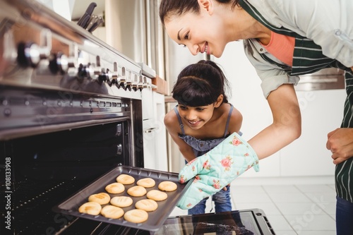 Mother and daughter placing cookies in oven photo