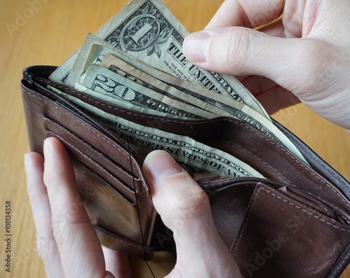 Male hand holding a leather wallet and withdrawing American currency (USD, US Dollars) 