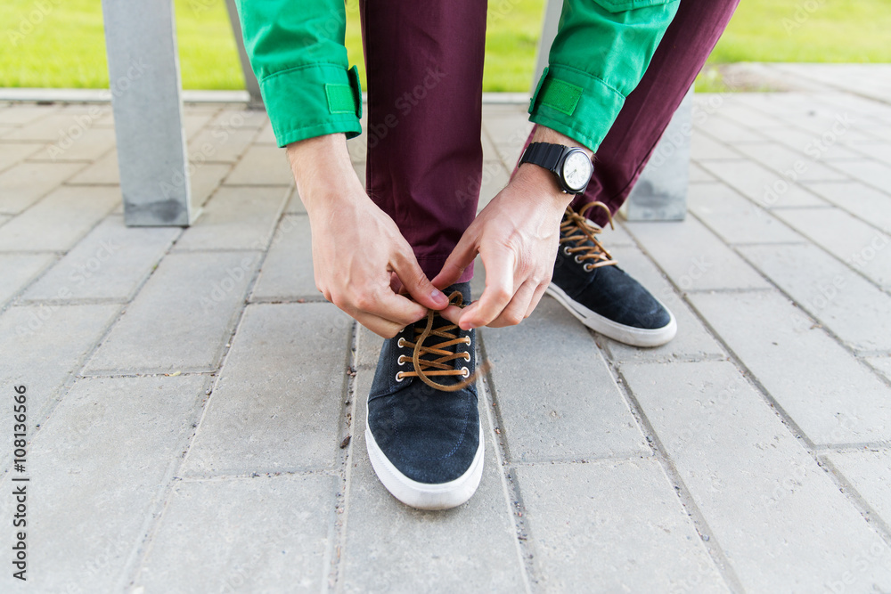 close up of male hands tying shoe laces on street