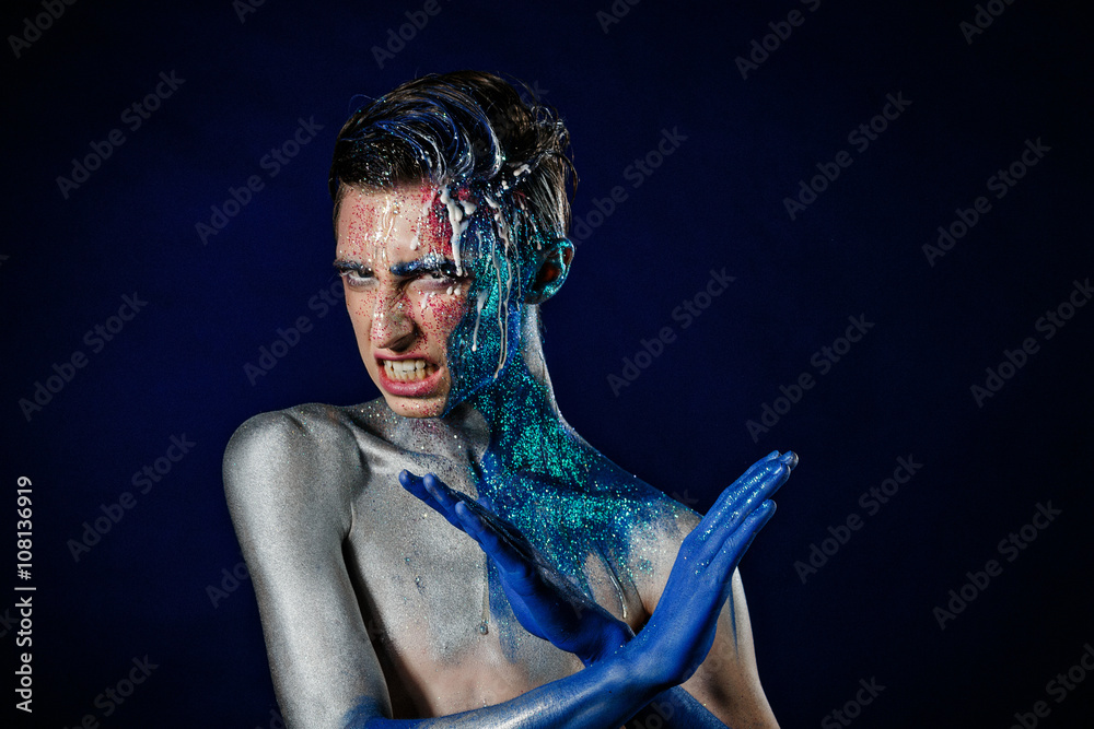 Crazy young androgyne man with face art. Freak person. Sperm on face. Tinsel creative blue makeup. Intersex and homosexuality concept. Space for logo