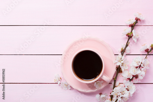 Cup of coffee and spring flowers on pink wooden table.