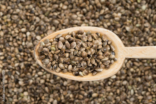 Wooden spoon with hemp seeds coming from right seen from above over a hemp seed background