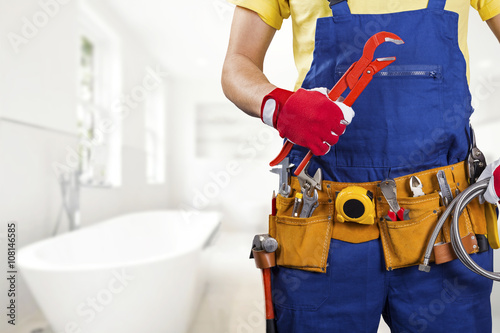 plumber with tool belt standing in bathroom photo