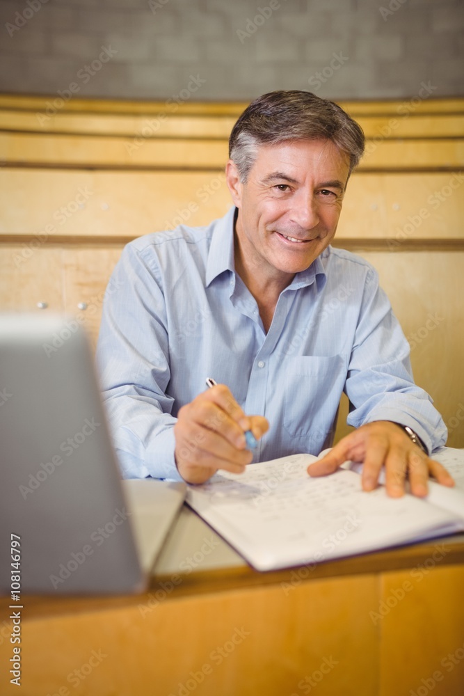 Portrait of happy professor writing in book at desk Portrait of happy professor writing in book at desk