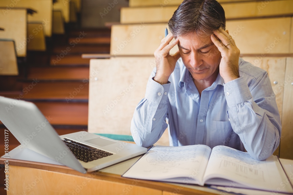 Obraz premium Depressed professor sitting with notes and laptop