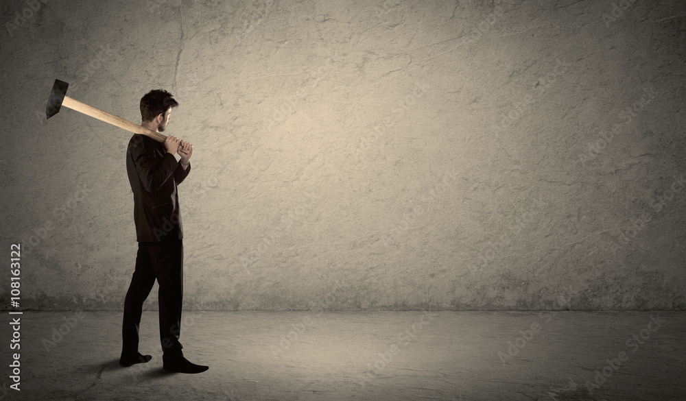 Business man standing in front of a grungy wall with a hammer Business man standing in front of a grungy wall with a hammer