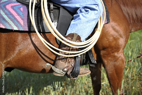 The rider's foot in brown cowboy boots in the stirrup and a coil of rope 