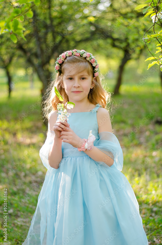 Little girl in blue dress under the blooming tree in spring garden Little girl in blue dress under the blooming tree in spring garden