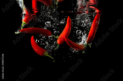 Several red peppers fallen into the water isolated on the black background
