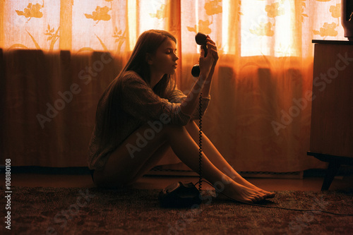 Caucasian woman sitting on floor staring at telephone photo