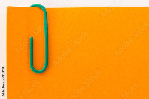 green paper clip on an orange sheet of paper macro