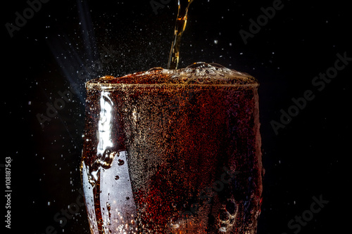 Soda large glass, overflowing glass of soda closeup with bubbles isolated on black background
